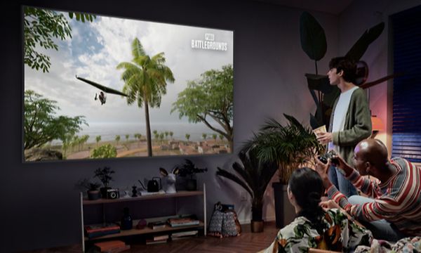 Tre personer i ett nedsläckt vardagsrum spelar videospel på en stor Samsung Neo QLED gaming-TV 