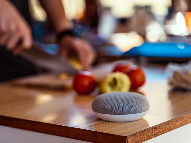 Google Nest mini på en köksbänk där någon skär upp äpplen i bakgrunden