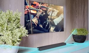 HT-A3000 trådlös sonudbar på en TV-bänk med växter under en TV som visar en stråkorkester och ljud som är illustrerat med blått