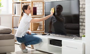 En person rengör en TV-skärm med en trasa (mikrofiberduk).