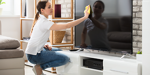En person rengör en TV-skärm med en trasa (mikrofiberduk).
