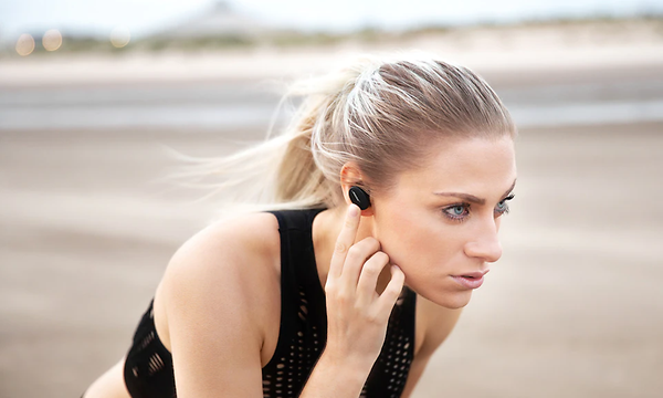 Blond kvinna med hästsvans och Bose in-ears hörlurar på en strand
