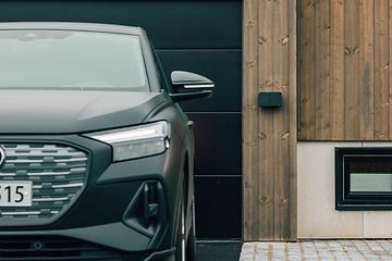 Väggmonterad Amina billaddare bredvid en bil som står parkerad framför ett garage