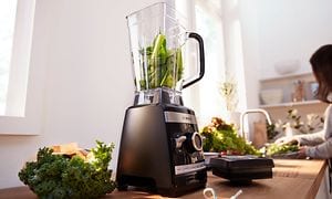 Bosch blender på en köksbänk, fylld med gröna grönsaker
