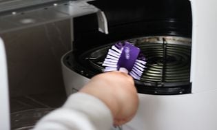  Person som rengör en airfryer med en lila diskborste