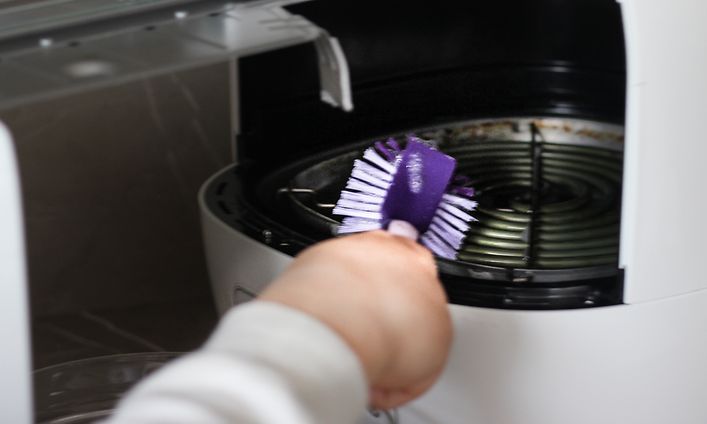 Person som rengör en airfryer med en lila diskborste