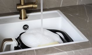 Airfryer med diskvatten i en vit, fyrkantig diskho och vatten som rinner ur en mässingkran. 