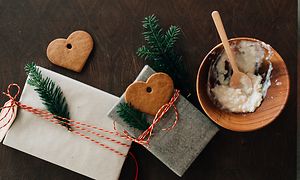 Två fint dekorerade julklappar, pepparkakshjärtan och en grötskål av trä med en sked i på ett bord
