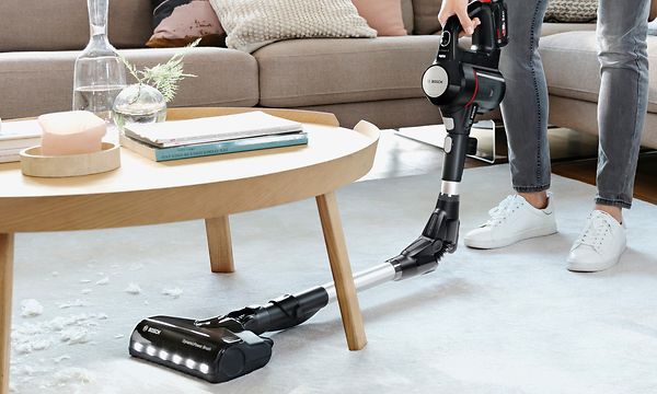 Kvinna städar med Bosch dammsugare och använder flex-röret för att rengöra under möbler
