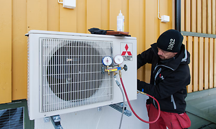 Man med svart mössa installerar utomhusenheten på en värmepump