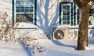 Utomhusenhet på en värmepump i snö utanför ett hus