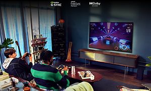 Två engagerade unga män sitter i ett ungdomligt vardagsrum och spelar bilspel på en stor TV-skärm framför dem 
