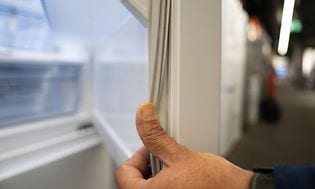 En man som kollar kvaliteten på en tätningslist på en kylskåpsdörr med tummen