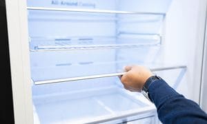 Man som håller i en kylskåpshylla i ett tomt och upplyst kylskåp