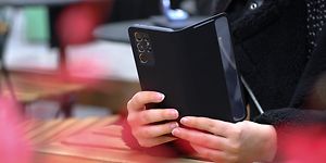 En kvinna håller en mobiltelefon med svart fodral med händerna på ett bord som står på en uteservering eller liknande