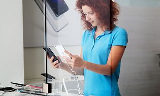 En kvinna med blå t-shirt jämför en svart och en vit telefon i en butik