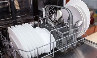 Nedersta hylla i en diskmaskin med rena, vita tallrikar och bestick
