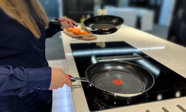 Kvinna i ett kök som håller två stekpannor över en spishäll