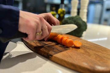 Kvinna skär upp morot på en skärbräda med broccoli i bakgrunden