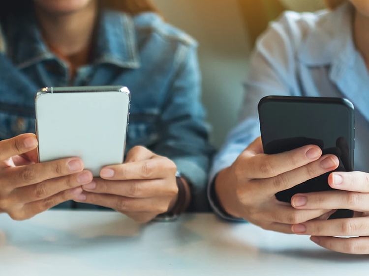 Tre ungdomar använder sina mobiltelefoner vid ett bord