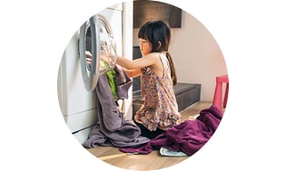 A young girl puts laundry into a washing machine