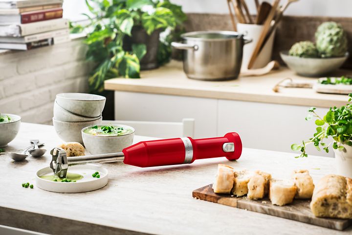 Röd Kitchen Aid stavmixer på en köksbänk bredvid en soppskål.