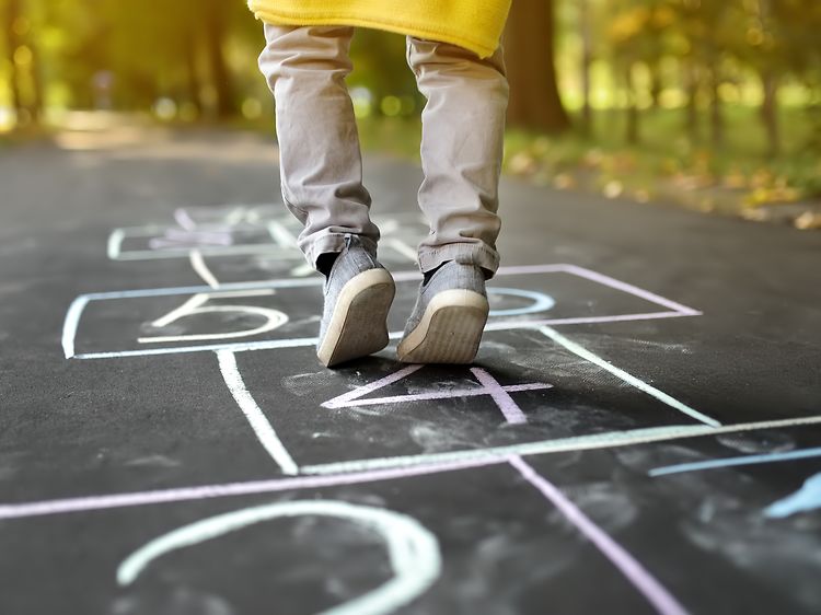 Barn och baby: Närbild av liten pojkes ben och "hoppa hage" ritad på asfalt.