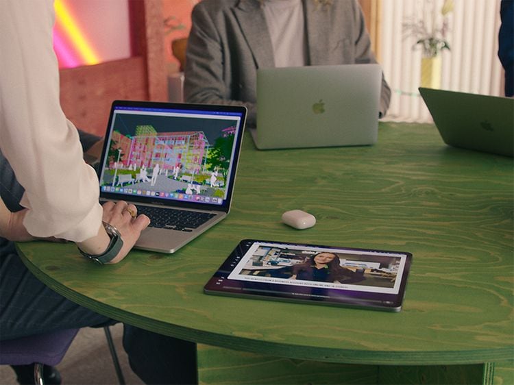 Grönt bord med MacBooks, iPad och Airpods