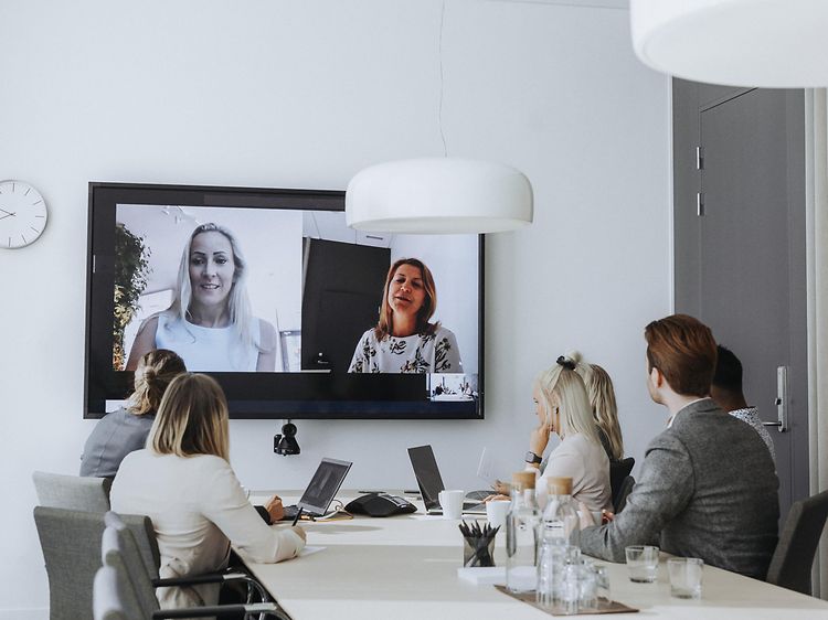 Office - B2B - people attending a hybrid meeting with laptops and a large screen