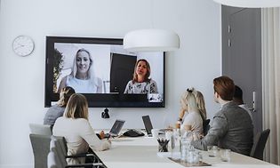 Office - B2B - people attending a hybrid meeting with laptops and a large screen