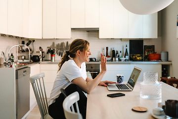 Woman sitting in front of a laptop waving to the webcam