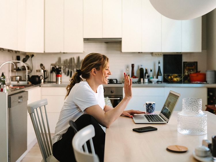 Woman sitting in front of a laptop waving to the webcam