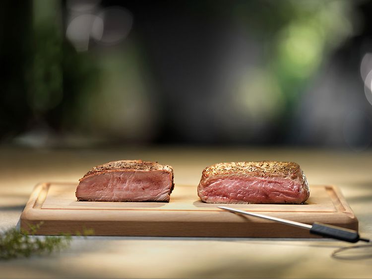 Two juicy pieces of meat on a cutting board and a knife next to it