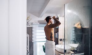 Man standing in a bathroom combing his hair after a shower and looking into a mirror