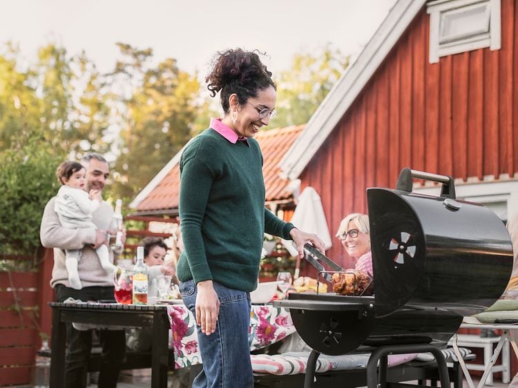 Woman grilling chicken on the grill, with her family in the background sitting around a table