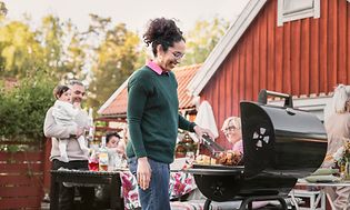Woman grilling chicken on the grill, with her family in the background sitting around a table