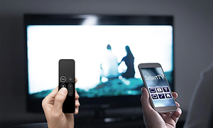 Fjärrkontroll till vänster och mobiltelefon med smart-tv app till höger framför en TV skärm.