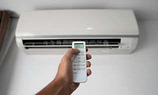Man's hand holding remote controller pointed towards heat pump
