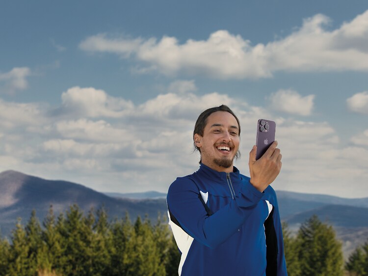 Man som håller en iPhone 14 Pro med naturlandskap i bakgrunden