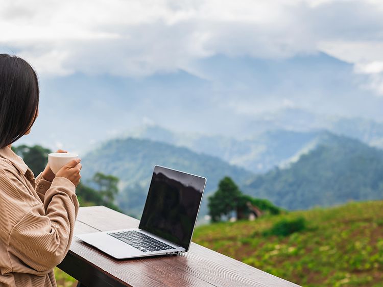 Woman with a laptop and computer staring on a view of nature and mountains