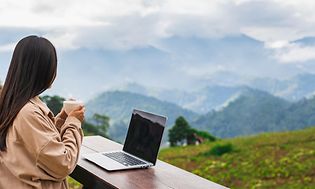 Woman with a laptop and computer staring on a view of nature and mountains