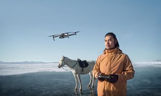 Man som flyger en DJI Air 2s-drönare i vinterlandskap bland snö och is, en vit häst står bredvid.