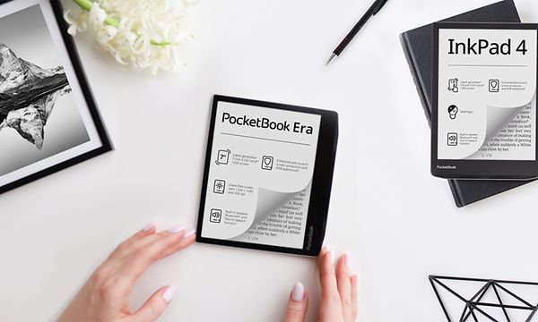 Pocketbook E-book reader surrounded by hands, a flower, picture of mountains and a black wire triangle