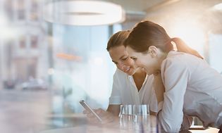 B2B - Telecom - Two women leaning on the table and looking at a phone