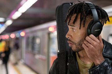 Young man at subway station wearing black Bose headphones