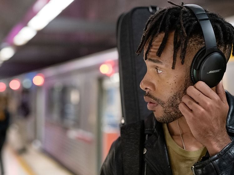 Young man at subway station wearing black Bose headphones