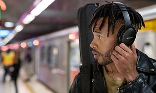 Young man at subway station wearing black Bose headphones