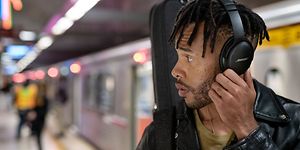 Young man at subway station wearing black Bose headphones