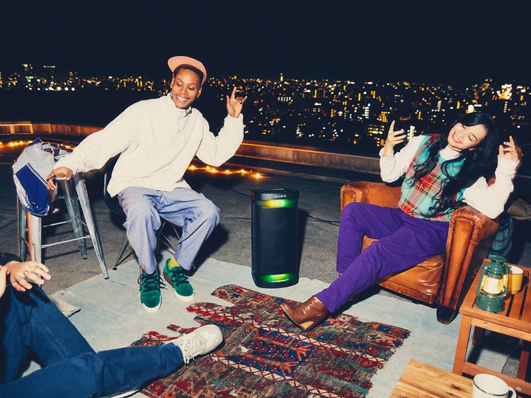 En kille och en tjej och en person till sitter på en balkong med på kvällen vid en högtalare och lyssnar på musik som de gillar