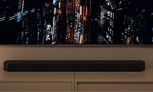 Samsung-soundbar under en TV-skärm som visar en storstad i kvällsmörker sett uppifrån